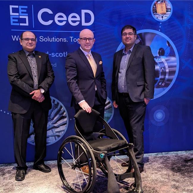 three men pose at an awards ceremony with a wheelchair