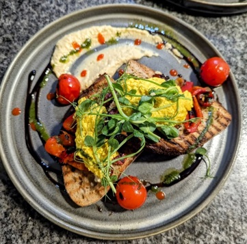 Vegan Fusion sourdough with chilli humus, scrambled red miso tofu, confit tomato and roasted red pepper presented on a plate