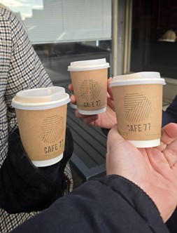 Three people holding 'Cafe 77' branded, brown takeaway cups